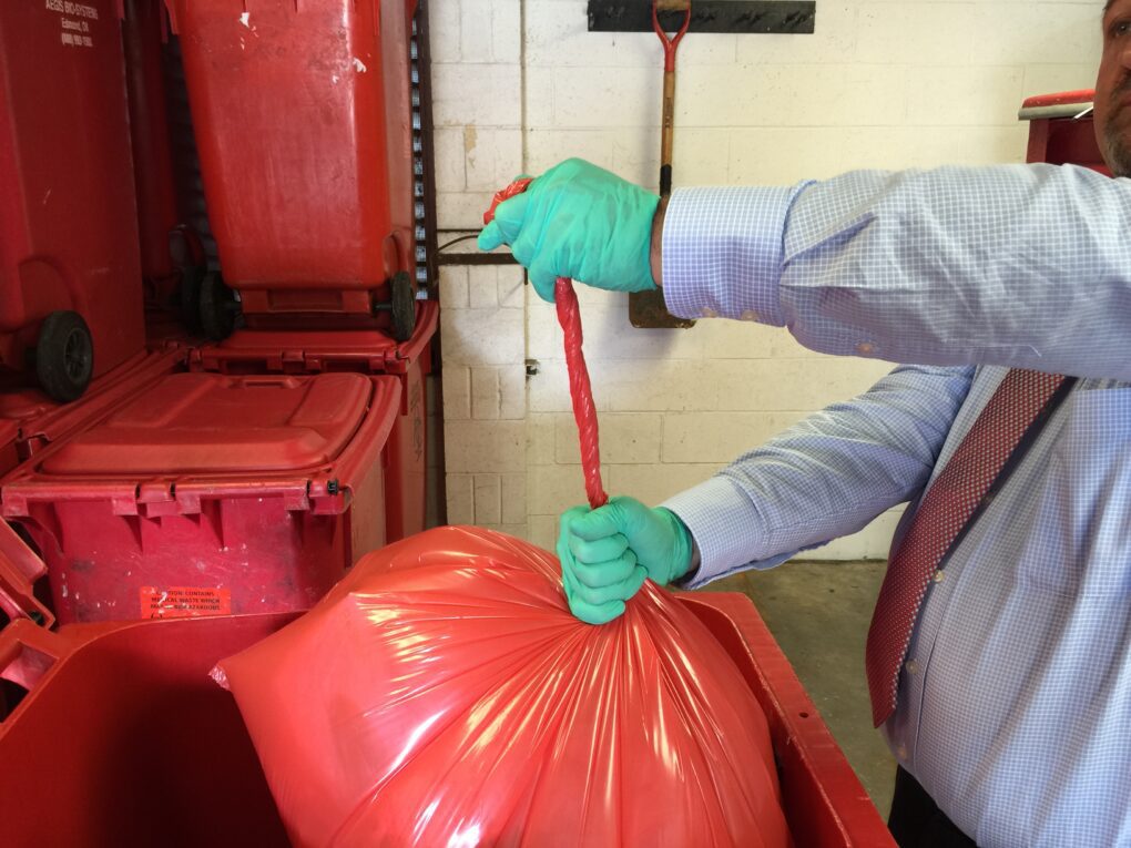 IMG_3364 1 | Advant-Edge Solutions of Middle Atlantic, Inc. Gloved worker secures red bag for disposal into medical waste containers and packaging bins.