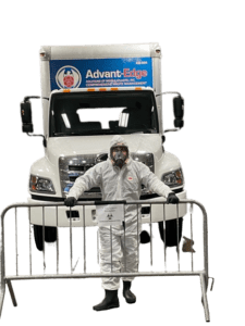 Image of ASMAI employee wearing a hazmat suit posing in front of the trucks with our logo on it