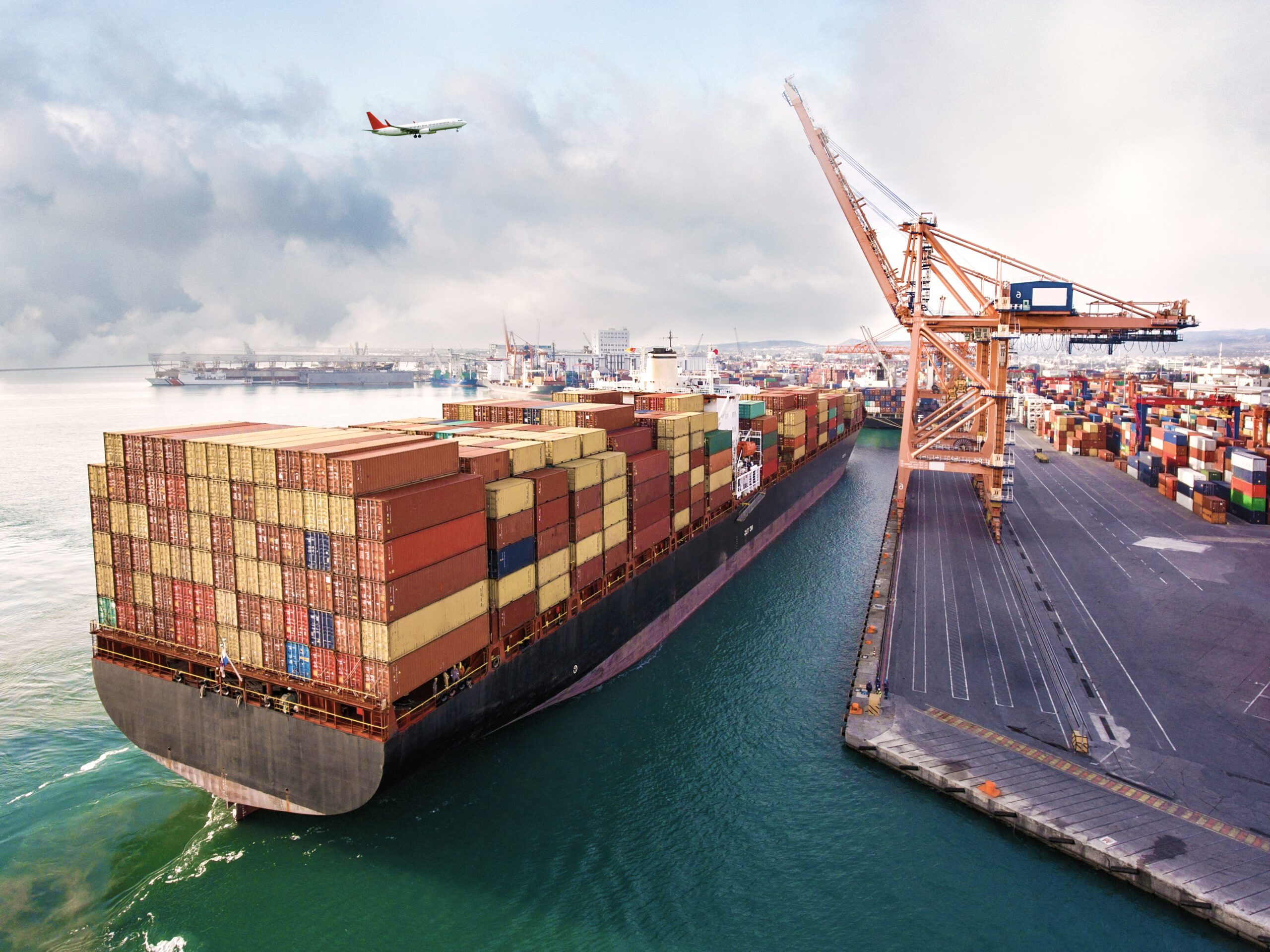 image of a container ship coming to shore and an airplane aboc in the sky