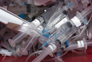 Used syringes and needles in a medical container illustrating the need for safe and compliant sharps disposal services.